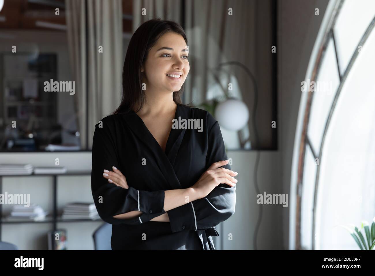 Happy young indian lady standing by window in good mood Stock Photo