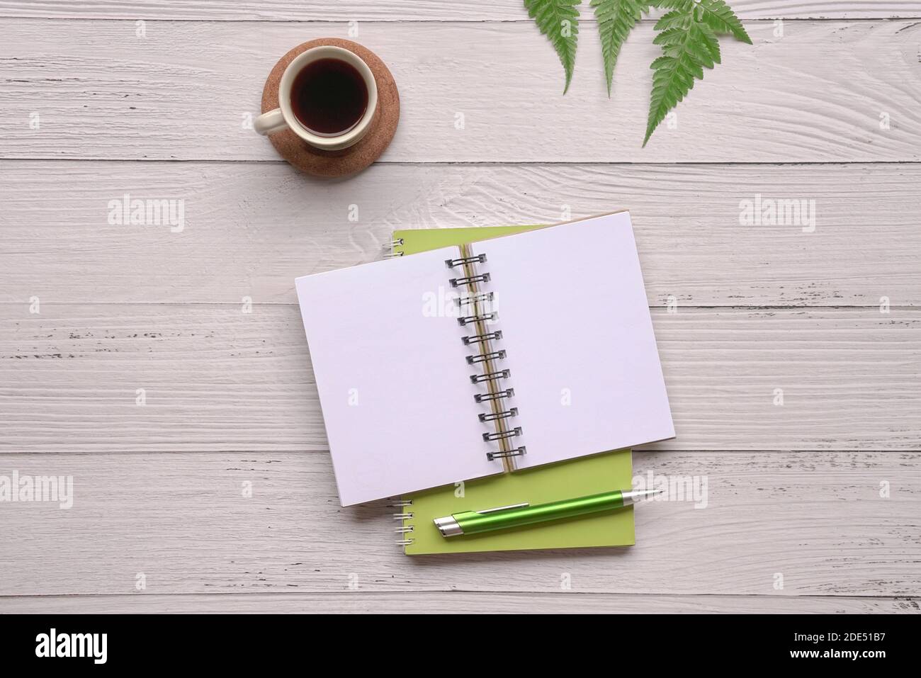 Open notepad with pen, coffee and green plants on wood table. Top view. Stock Photo