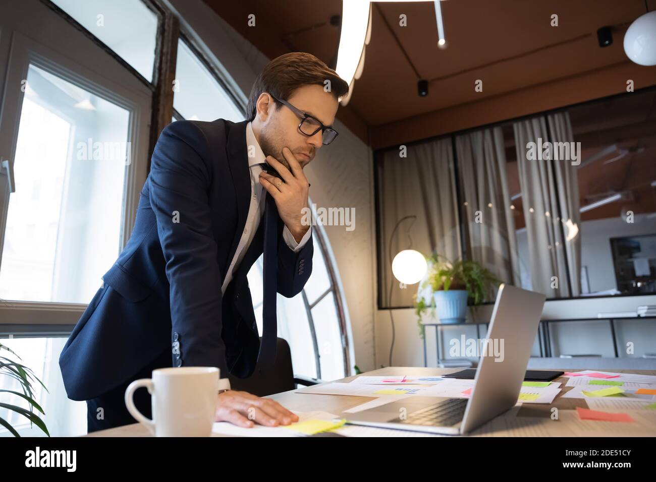 Male executive standing by table studying data on laptop screen Stock Photo