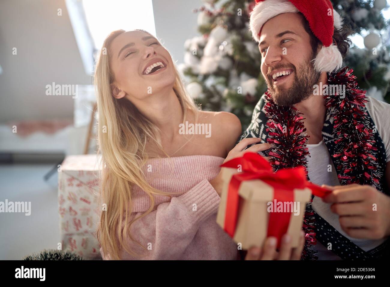 happy young caucasian couple having fun while opening christmas presents, laughing Stock Photo