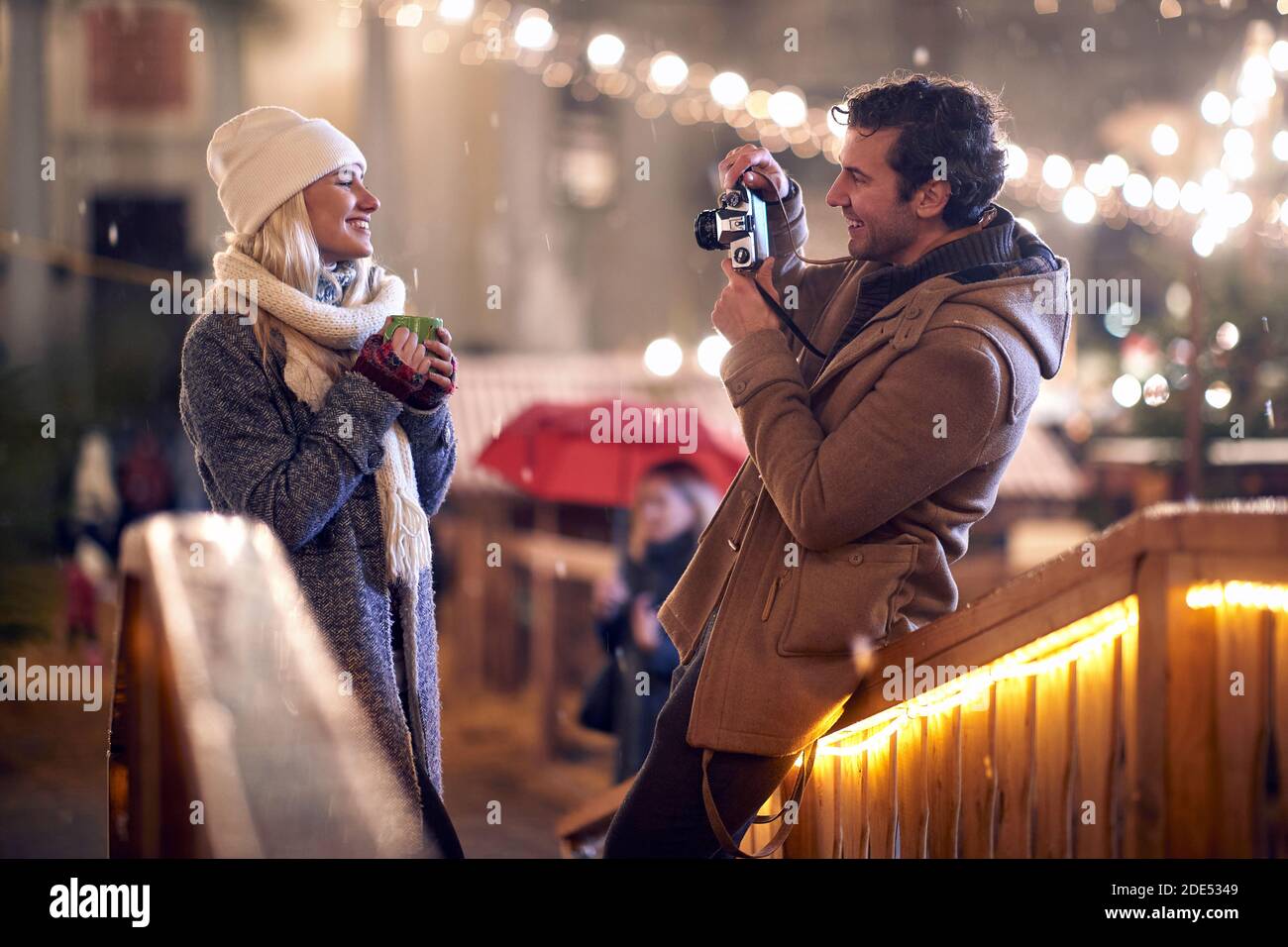 young caucasian man taking a photo of his girlfriend holding cup of tea outdoor with retro camera Stock Photo
