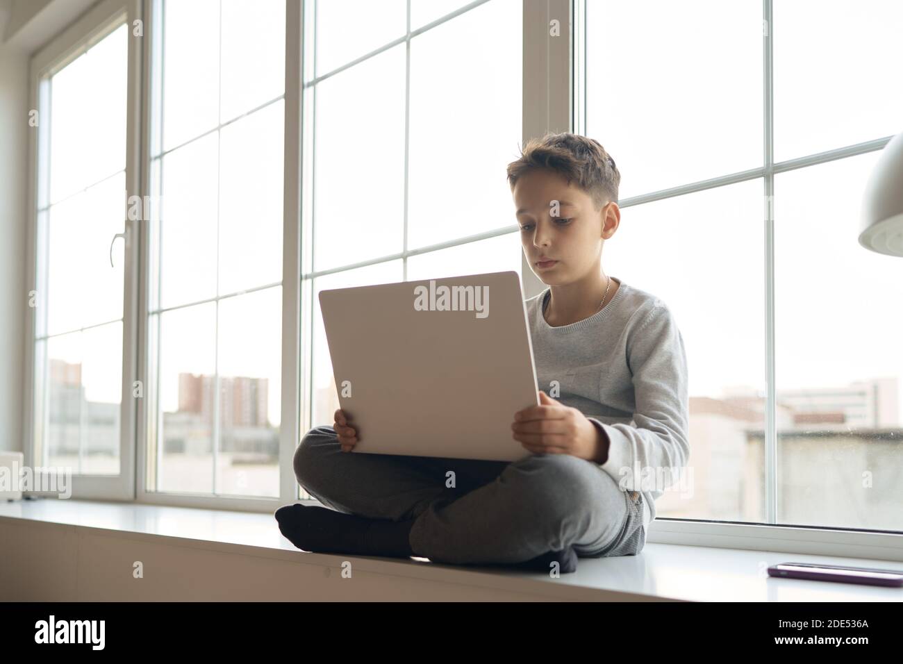 Schoolboy sitting on sill of big white window and pushing button on ...