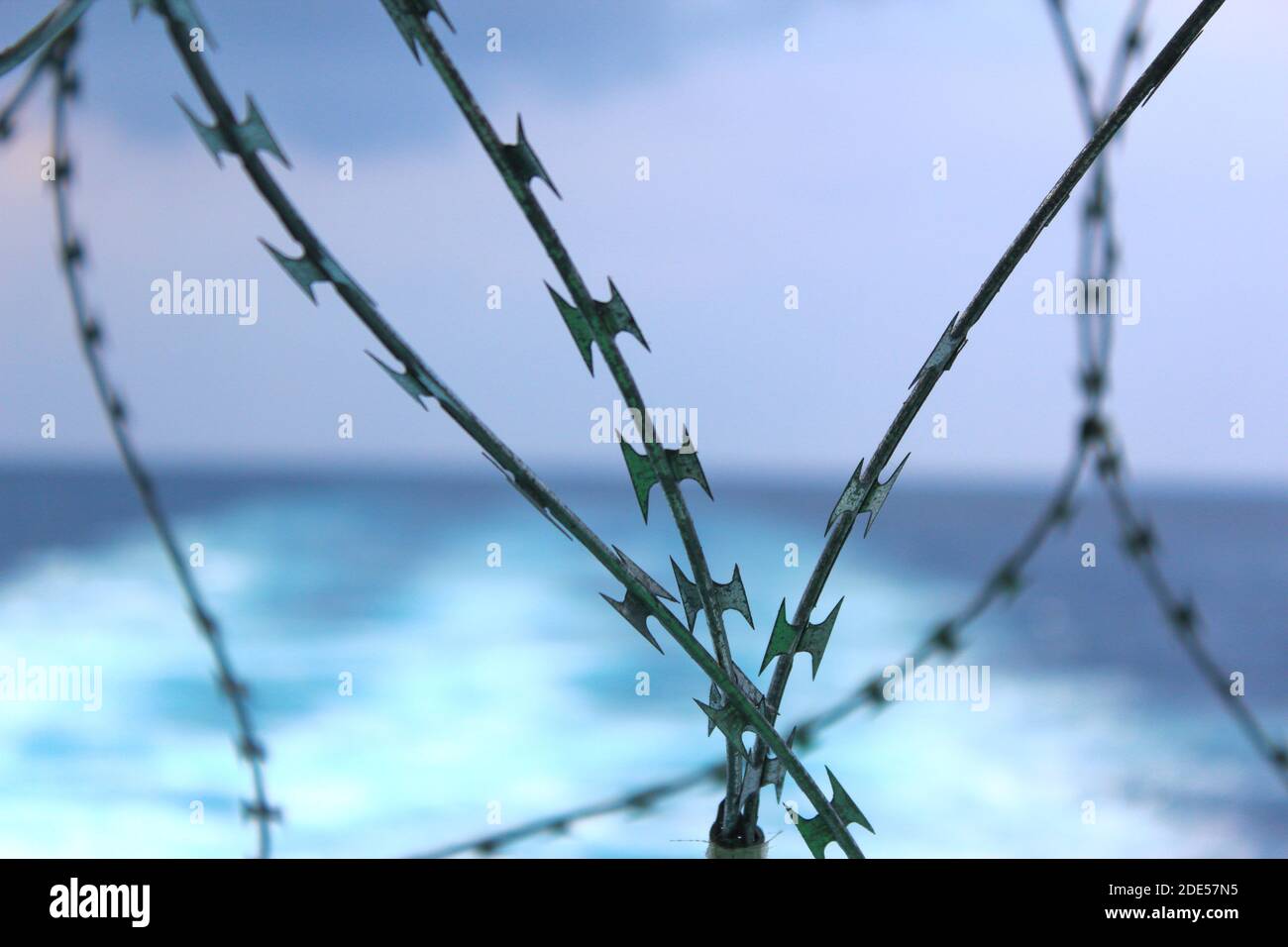 Close up shot of NATO razor wire on a ship with a blurred ship wake and blue ocean in the background. Stock Photo