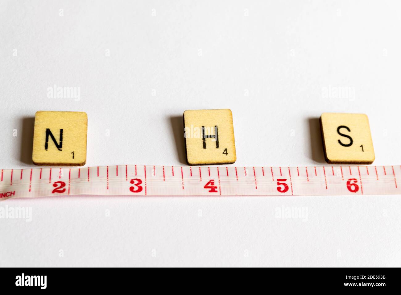 Old worn vintage wooden textured cubes with letters spelling NHS and tape measure depicting the government guidelines to social distance 2 meters to s Stock Photo