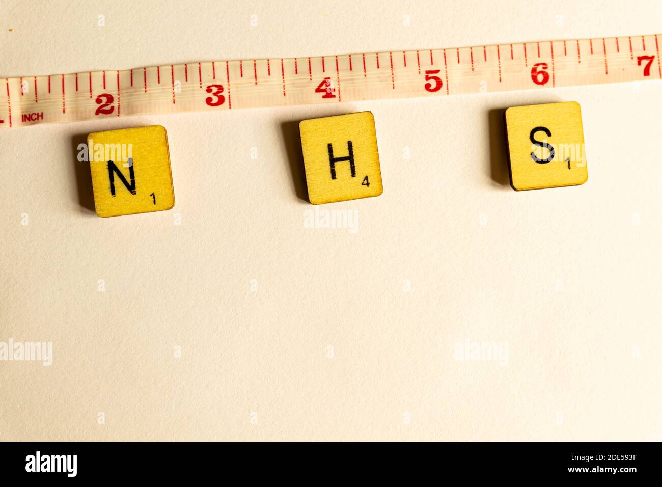Old worn vintage wooden textured cubes with letters spelling NHS and tape measure depicting the government guidelines to social distance 2 meters to s Stock Photo