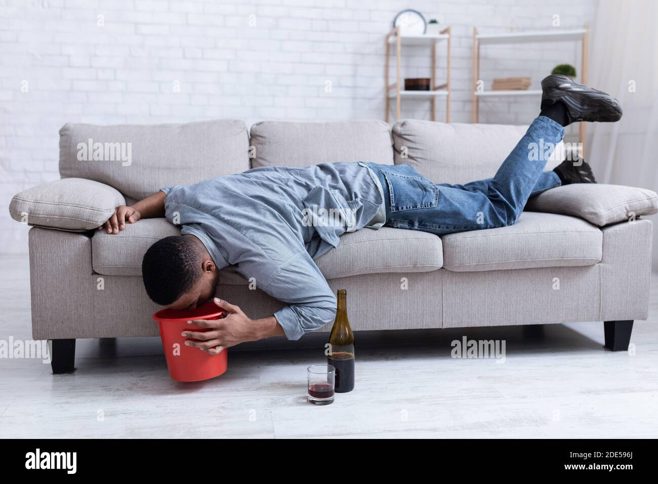 Drunk Man Vomiting Into Bucket After Drinking Wine Lying Indoor Stock Photo