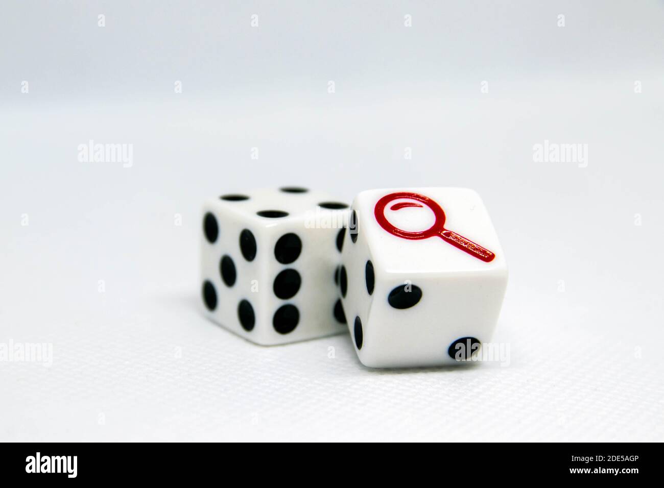 Pair of die with one showing black dots and one showing a red detectives magnifying looking glass. Isolated. Concept for mystery, strategy, luck, Stock Photo