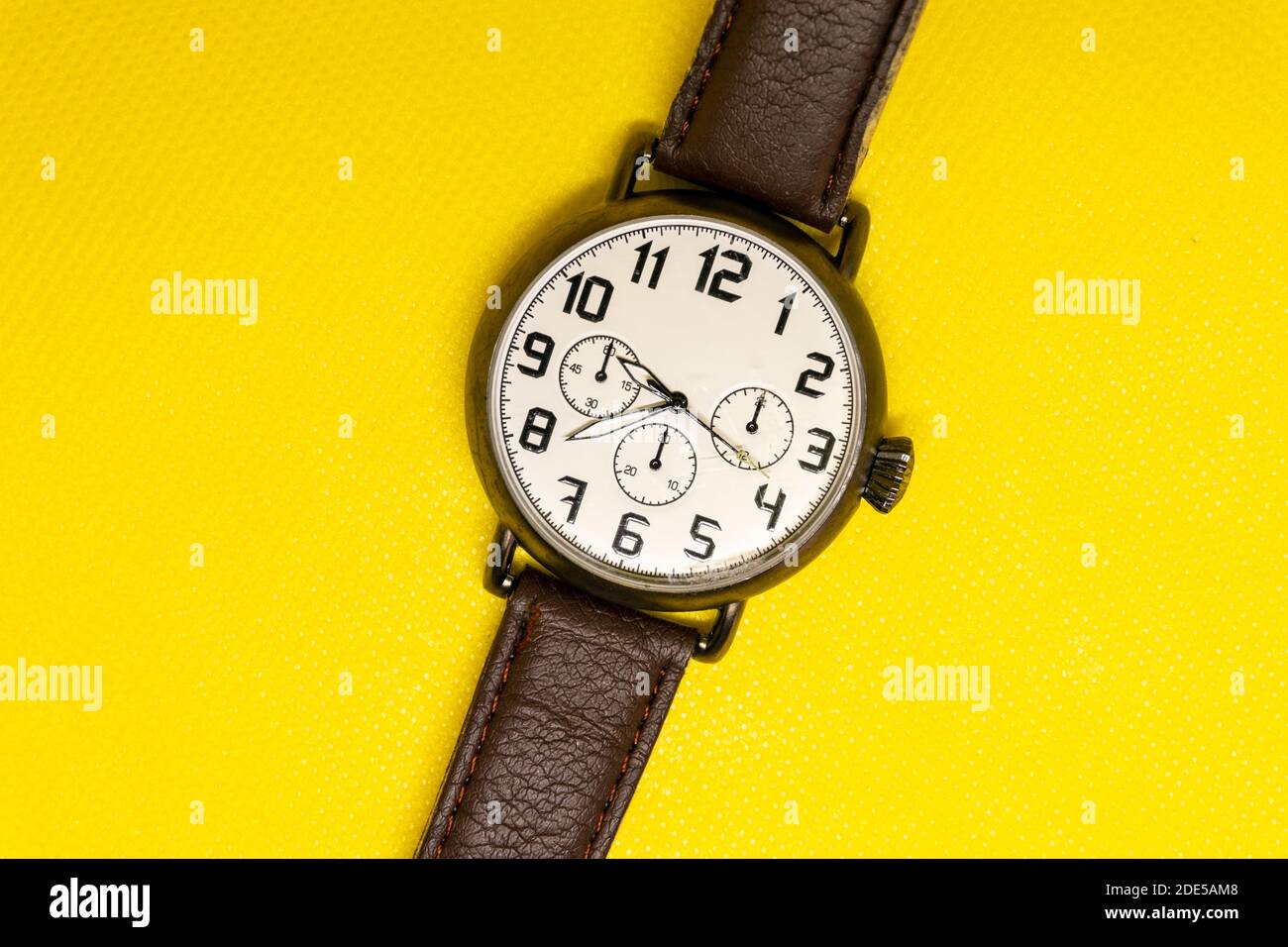 Rustic wristwatch with large watch face and leather stapes. Casual, fashionable and vintage brown male watch on yellow isolated background. Copy text Stock Photo