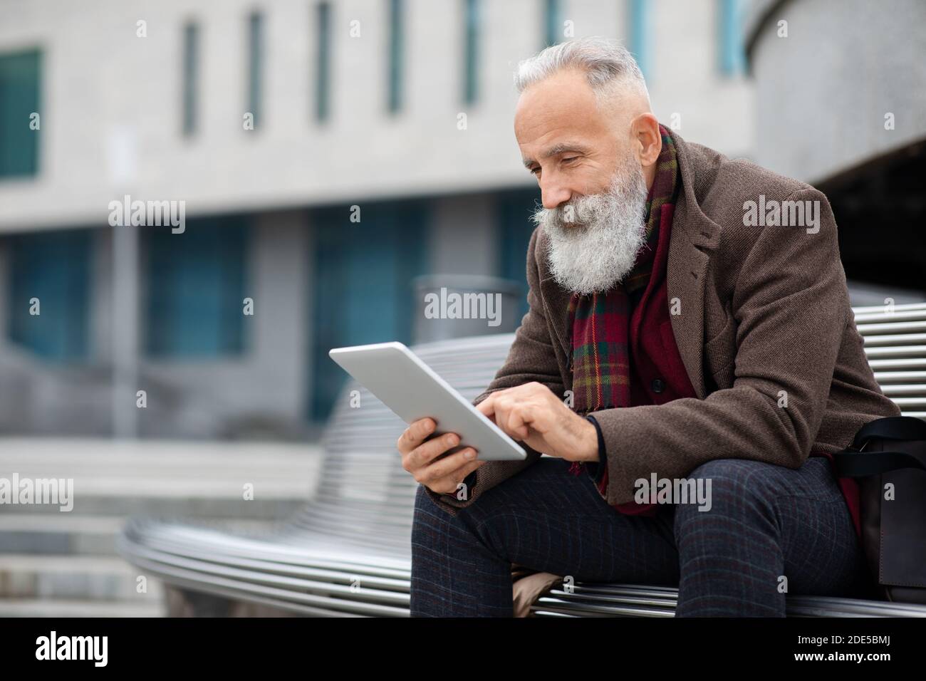 Stylish grey-haired man sitting on the bench, using digital tablet Stock Photo