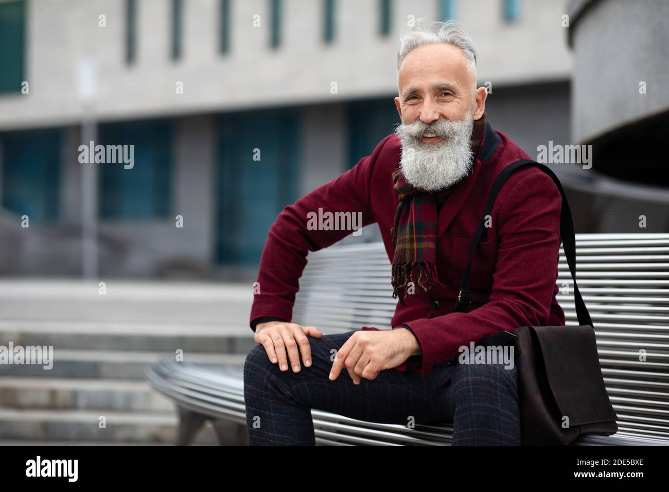 Handsome aged man sitting on bench, smiling at camera Stock Photo