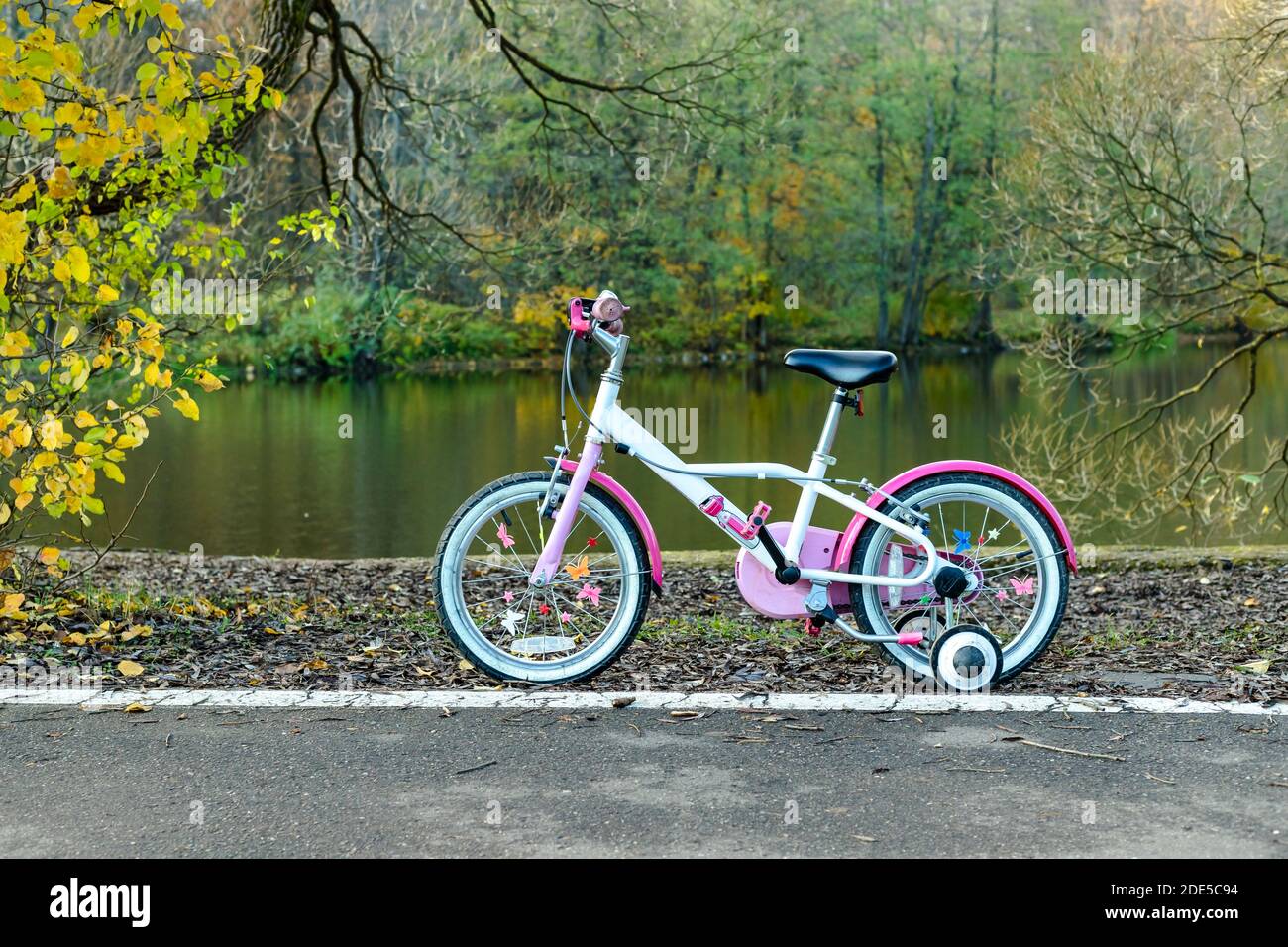 Childrens girls bicycle stands on path near pond at park under trees on autumn natural background Stock Photo