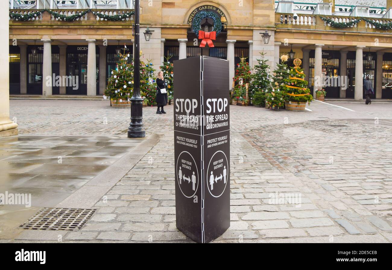 View of a Stop The Spread Of Coronavirus sign in Covent Garden with Christmas trees in the background. Stock Photo