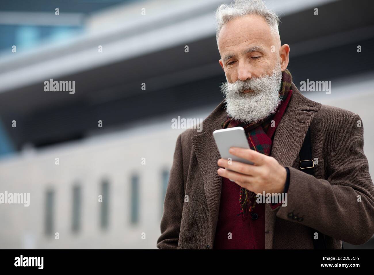 Grey-haired businessman using smartphone on the street Stock Photo