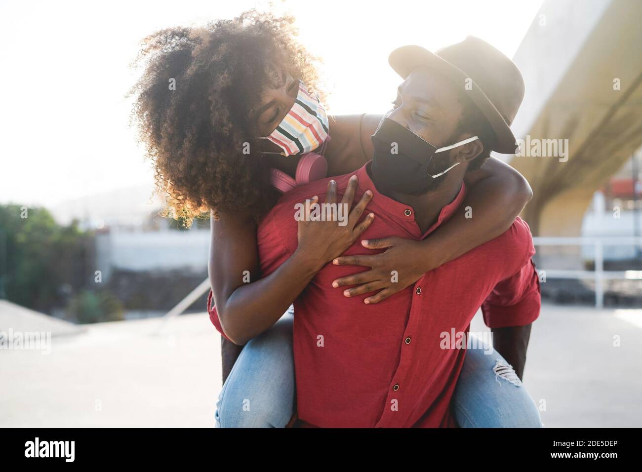 African couple having fun outdoor wearing safety masks during Coronavirus outbreak - Covid 19 lifestyle - Focus on woman face Stock Photo