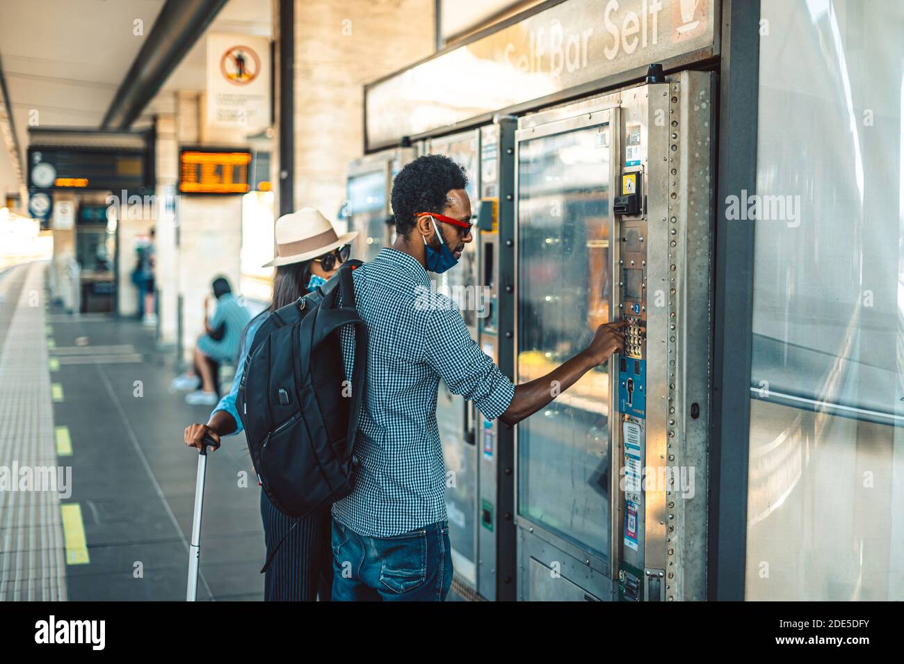 Black couple choosing beverage and food in vending machine at train station - Man and girl wear surgical mask selecting soft drink at modern beverage Stock Photo