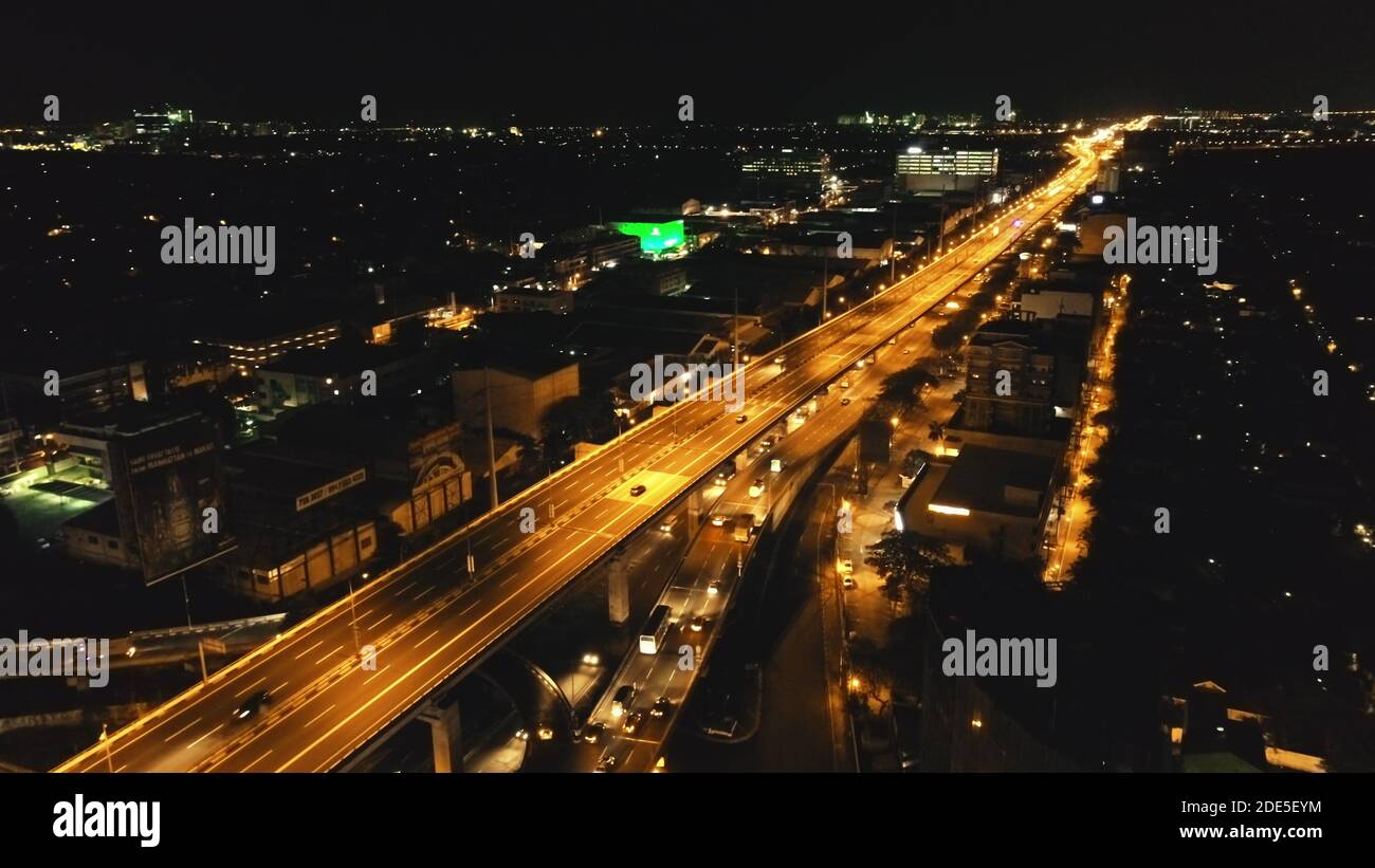 Closeup night traffic highway with driving cars, vans, trucks aerial view. Urban cityscape of Philippines metropolis of Manila close up. Modern buildings with bright illuminated road on bridge Stock Photo