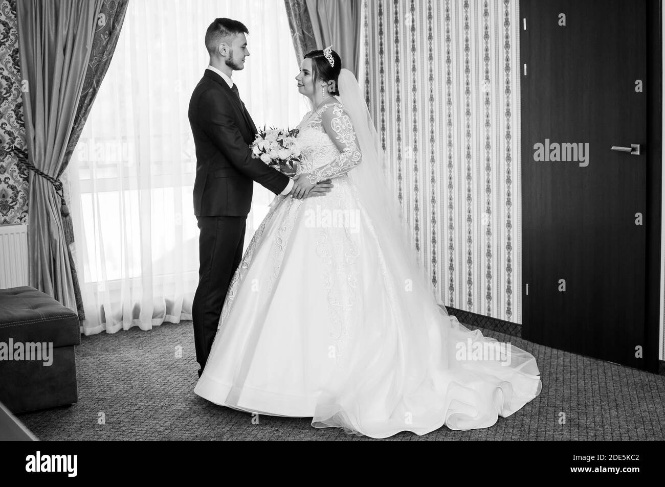 the groom looks at the bride and holds hands in the hotel room Stock