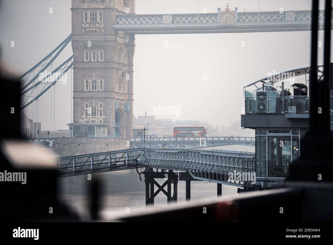 Red London Bus driving over Tower Bridge and River Thames in foggy misty weather in London City Centre on Coronavirus Covid-19 lockdown day one, England, UK Stock Photo