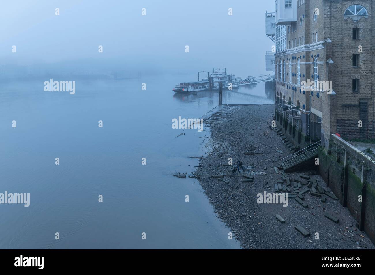 Butlers Wharf Pier at low tide with a River Thames beach in thick foggy and misty moody weather in London city centre during Covid-19 Coronavirus lockdown, England, UK Stock Photo