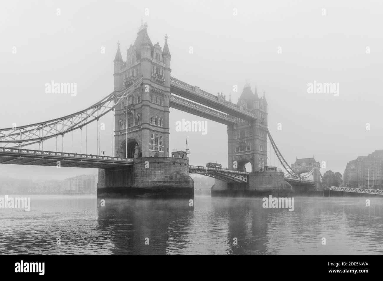 Black and white Tower Bridge and London Bus driving over River Thames in foggy and misty atmospheric, moody weather on Coronavirus Covid-19 lockdown day one, England, UK Stock Photo