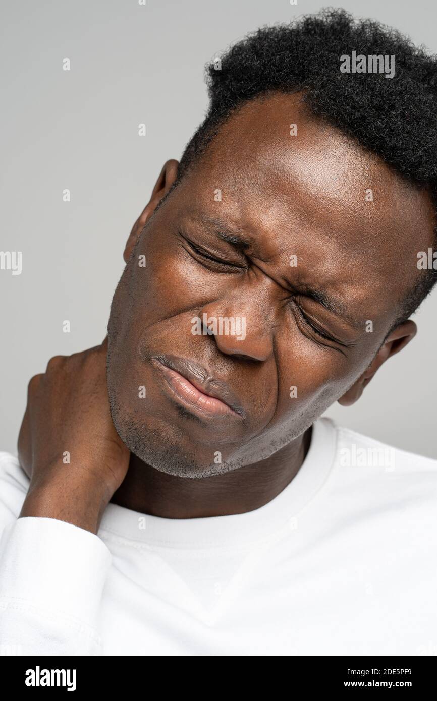 Frustrated Black man holding hand on his neck, closed eyes, suffers from pain and pinched nerve in forearm, massages tense back muscles, isolated on s Stock Photo