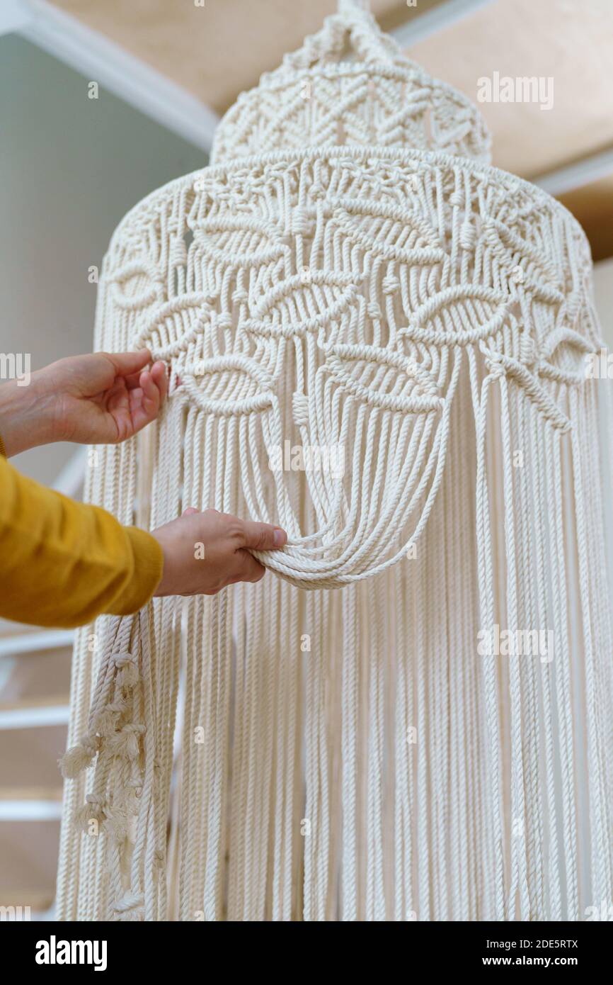 Freelancer woman working on half-finished macrame piece, weaves lamp shade for chandelier. Women hobby. Stock Photo