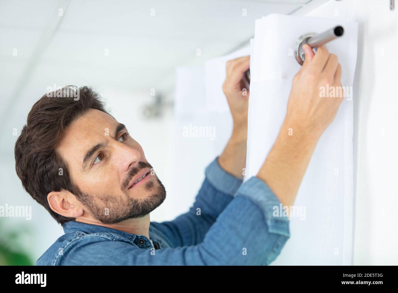 man hanging window curtain indoors Stock Photo
