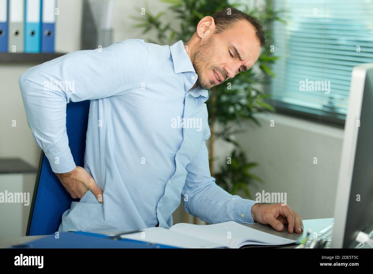 man with back pain in armchair at office Stock Photo - Alamy
