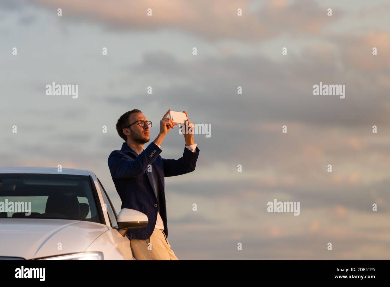 Man driver stopped to take a photo of sunset with mobile smart phone. Summer time. Stock Photo