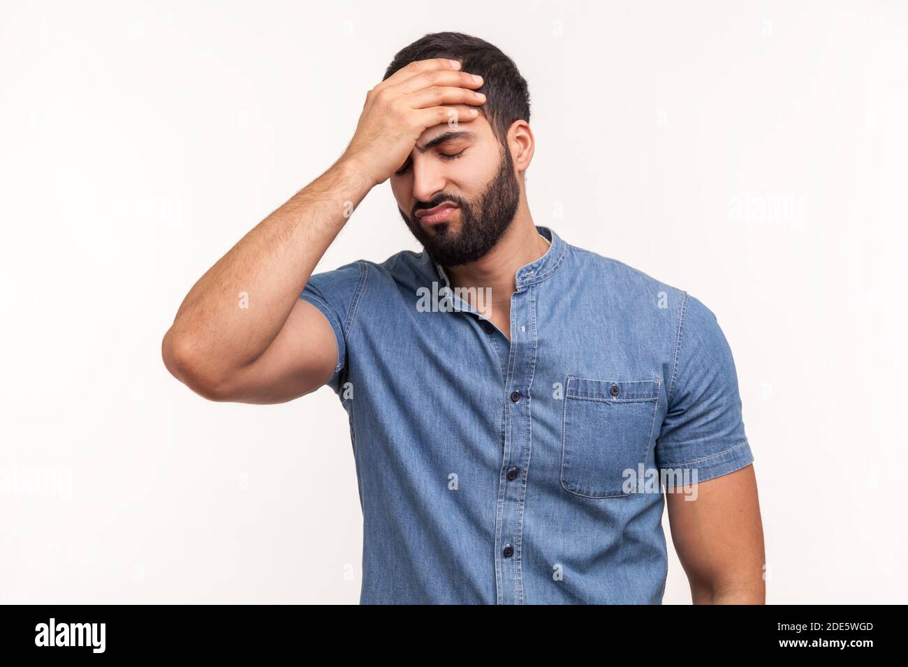 Upset frustrated man holding forehead with hand, making facepalm gesture, lost all his money, forget about date, big failure. Indoor studio shot isola Stock Photo