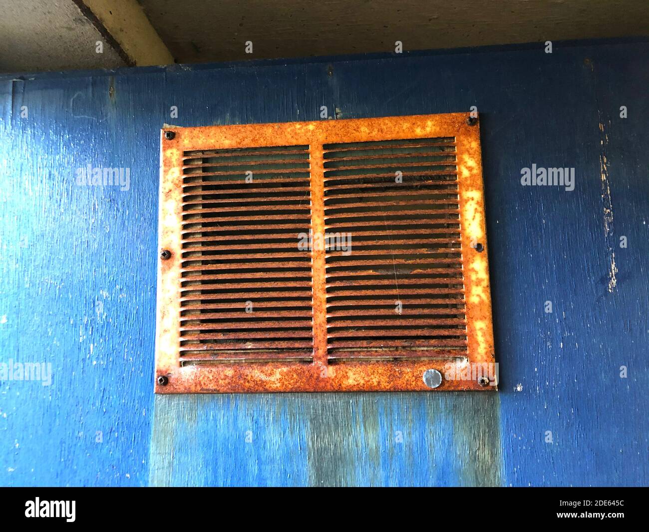 a close up view of a rusted airvent on a solid blue door Stock Photo