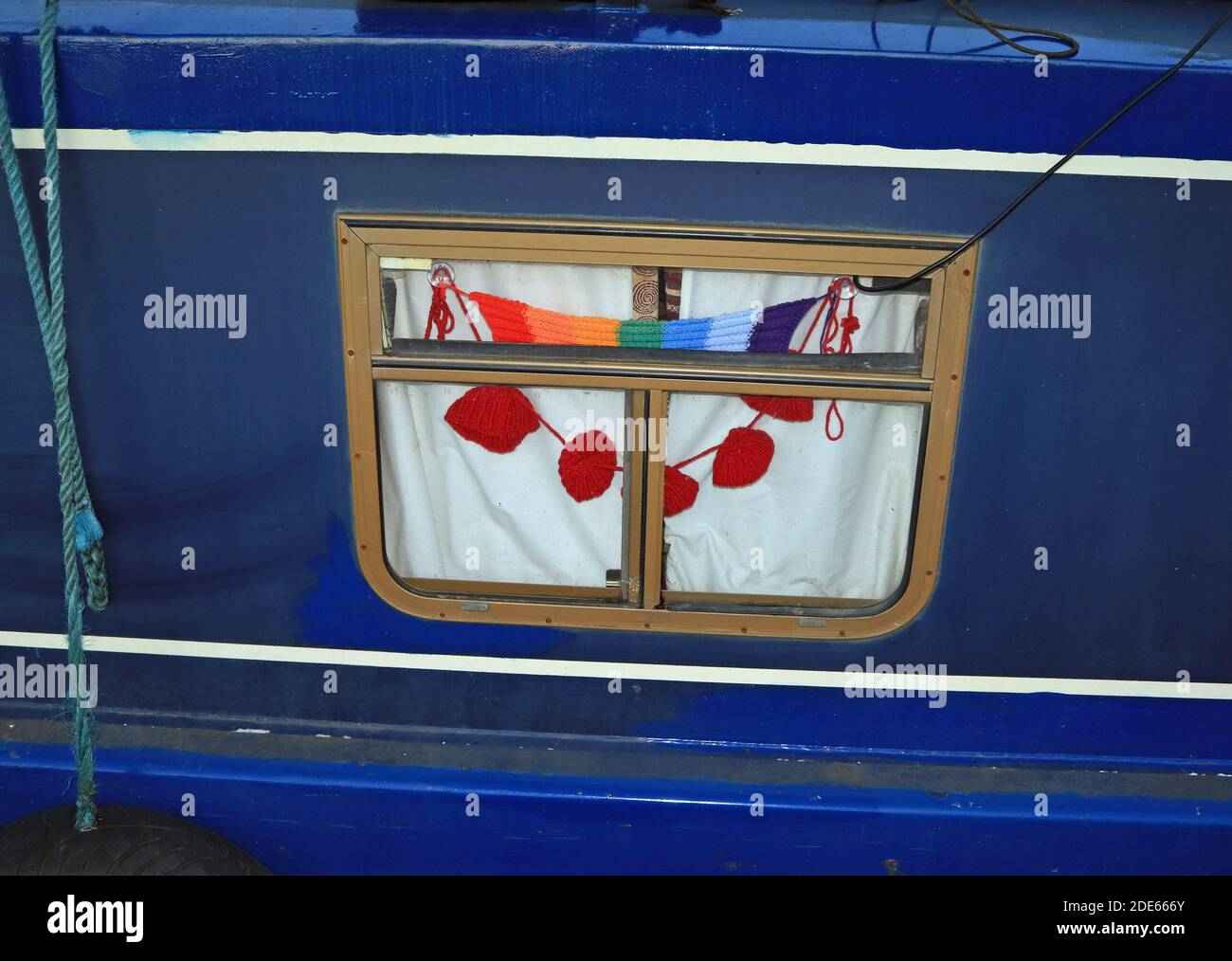 Hand knitted poppies and a rainbow scarf in a canal narrow boat window hung in remembrance of the fallen and in appreciation of fallen and NHS heroes Stock Photo