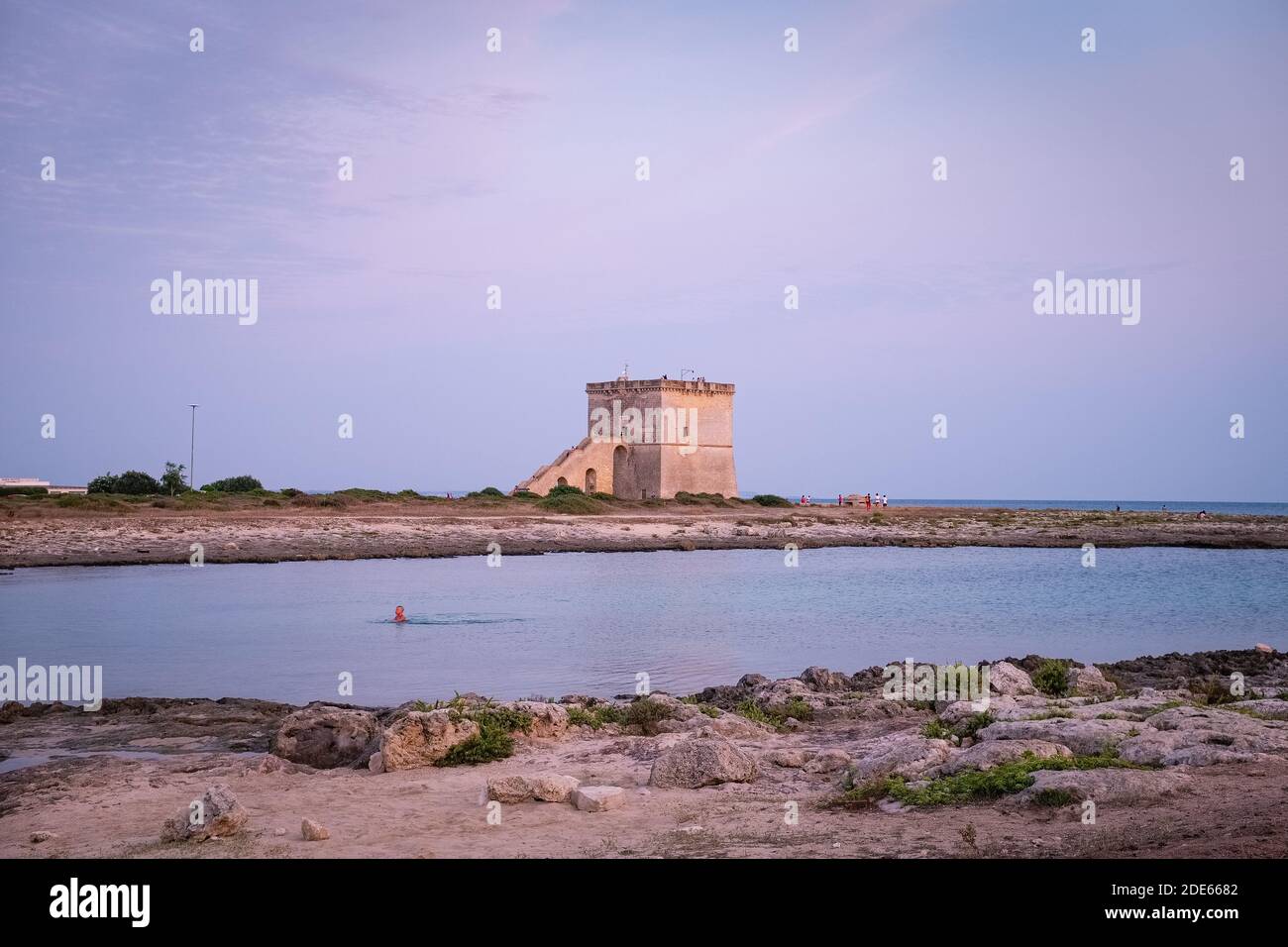 PORTO CESAREO, ITALY - SEPTEMBER 4, 2019: View of the ancient defensive  coastal tower Torre Lapillo at the sunset with a boy swimming in the sea. Pug Stock Photo