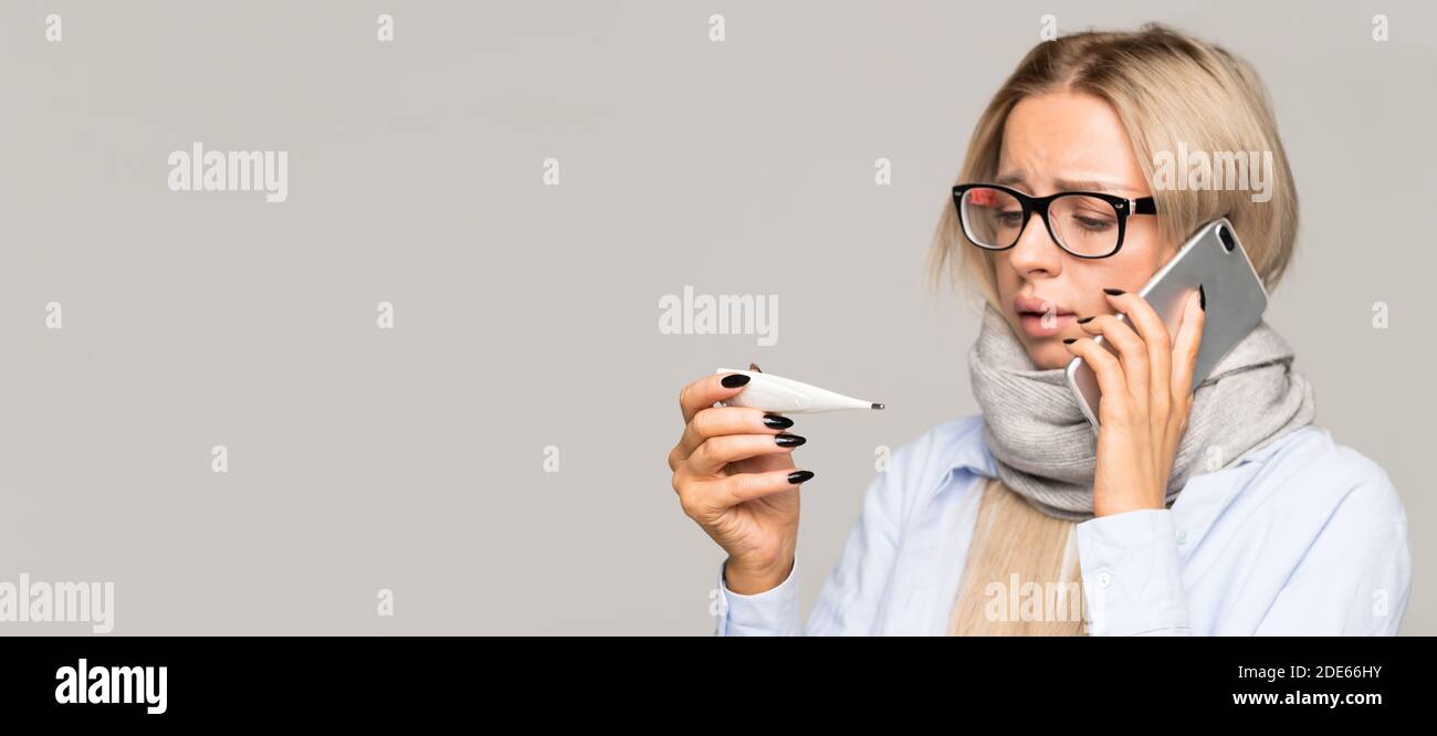 Sick young woman with glasses caught cold, looking at thermometer, talking on mobile phone. Cold, flu season Stock Photo