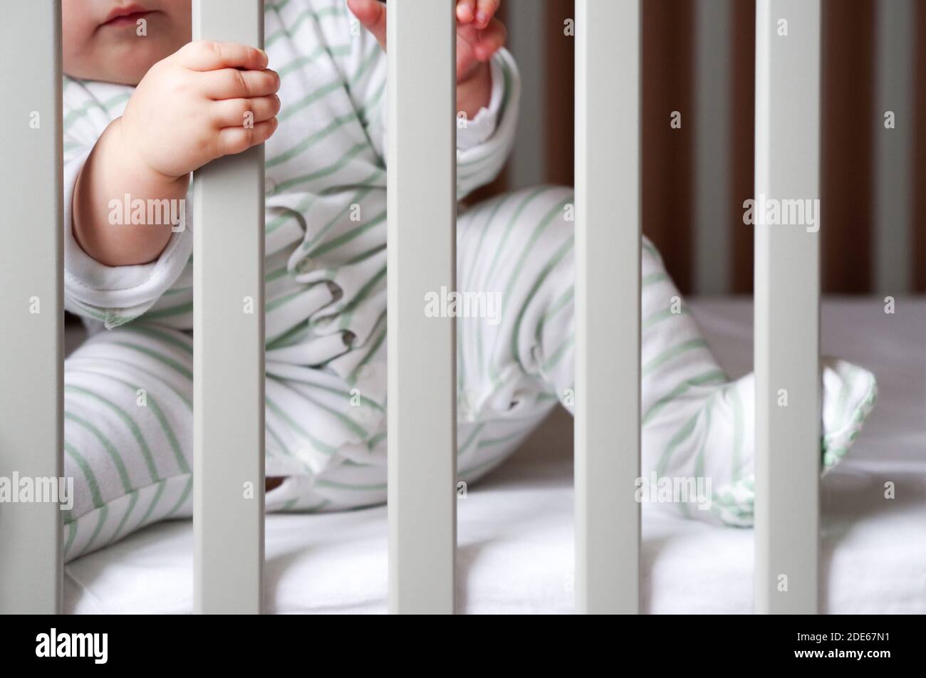 Chubby baby in a cot bed holding on to the bars Stock Photo