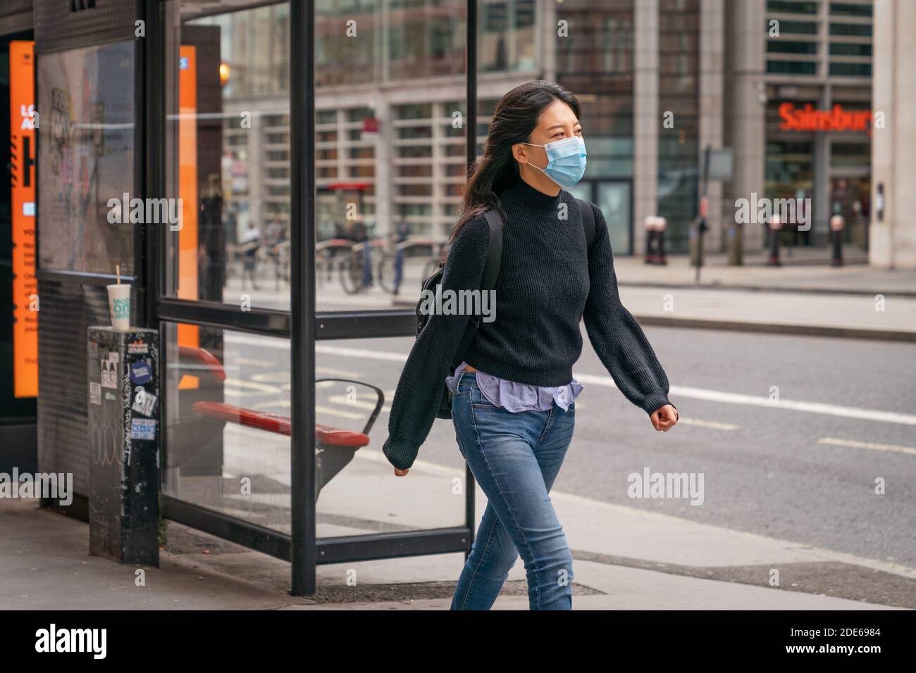 LONDON, ENGLAND - October 23, 2020 - Beautiful chic young smiling oriental woman with long hair walking on High Holborn in London wearing a face mask Stock Photo