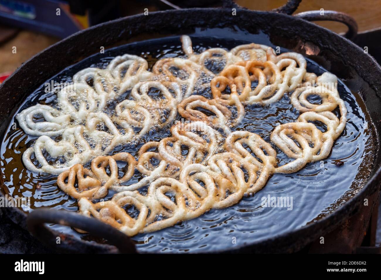 Frying Jalebi batter in oil. Red and orangecolored batter will be
