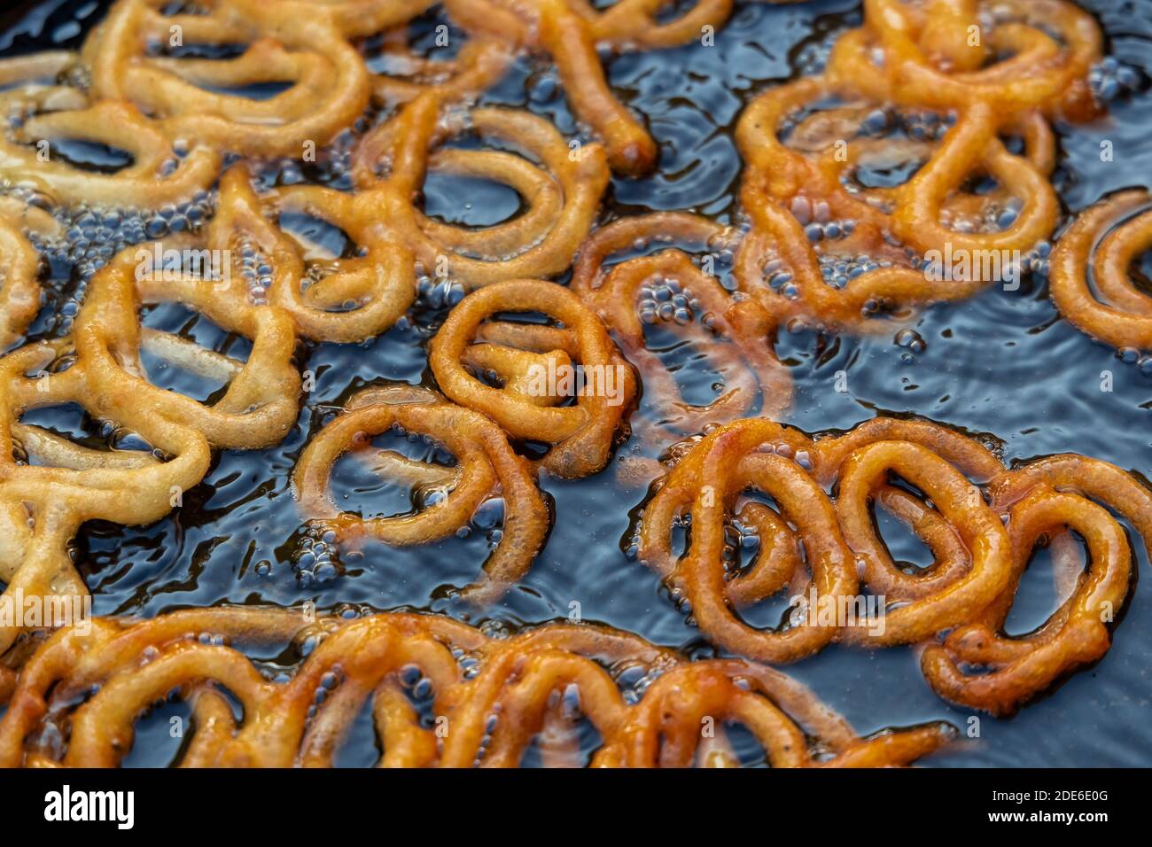 Frying Jalebi batter in oil. Red and orangecolored batter will be