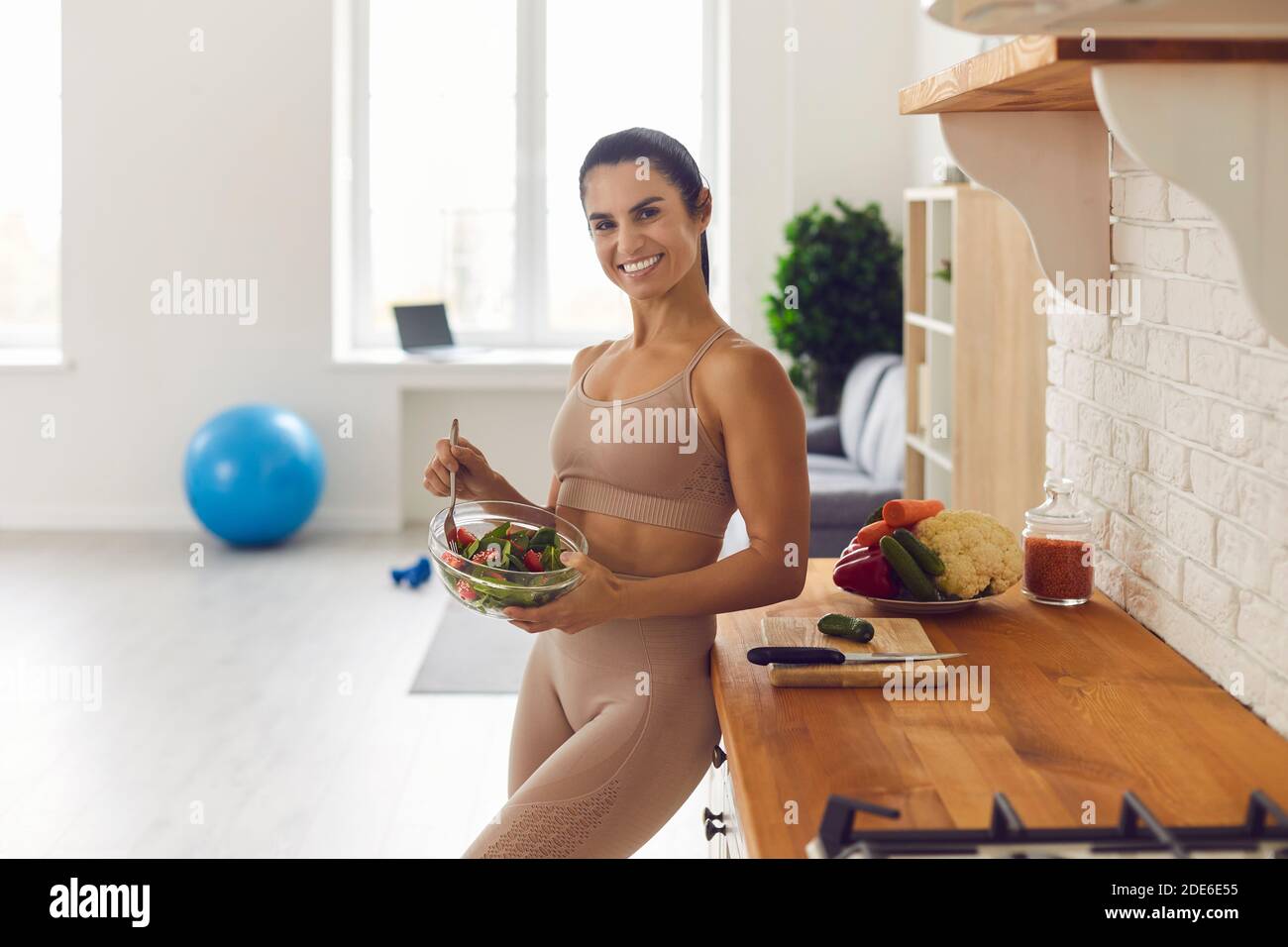 Happy athletic woman eating healthy vegetable salad after fitness workout at home Stock Photo