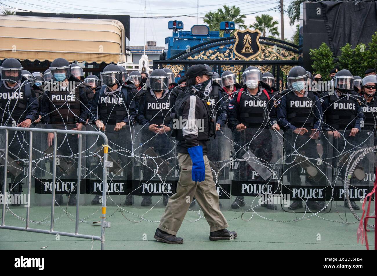 A volunteer guard walks past the riot policemen during the demonstration. Thousands of pro-democracy protesters gathered at BTS wat phra si mahathat where they marched to the 11th Infantry Regiment (King's guard) to oppose the legislation to control over some army units by King Maha Vajiralongkorn and call for monarchy reforms. Stock Photo