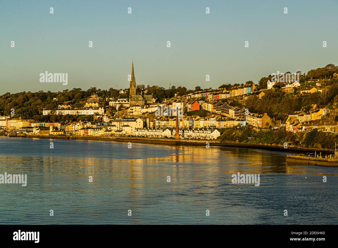 St Colman's Cathedral, its 91-metre spire towering over the colourful terraced houses of Cobh, County Cork, Ireland, seen here from the water in the morning light. Built between 1868 and 1919 in the Gothic Revival style (architects Edward Welby Pugin and George Ashlin), the cathedral holds the largest carillon in Ireland and Britain, with 49 bells. Cobh, formerly known as Queenstown, was the Titanic's last port of call in 1912. Stock Photo