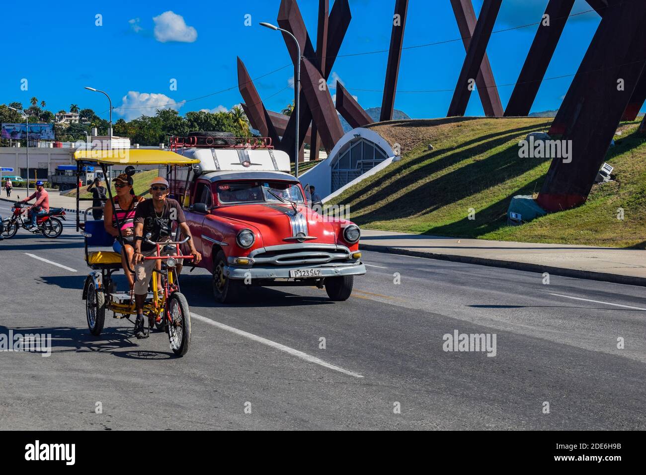 Bici-taxi and car driving past plaza de la revolucion - Santiago de Cuba - Cuba Stock Photo
