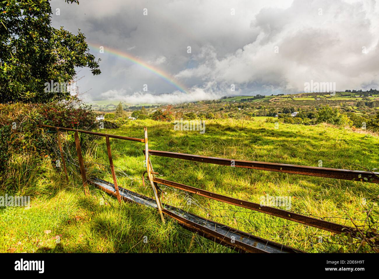 A rainbow stretches across pastureland and forest near the border of County Cork and County Kerry, Ireland, on the drive towards Killarney and the Gap of Dunloe. Stock Photo