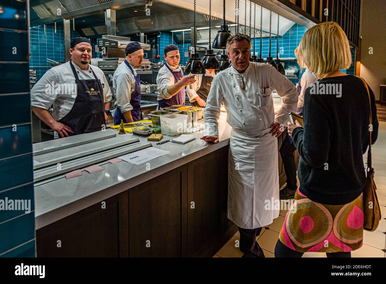 Chef Jupp Osterloh talks with his kitchen team in the open kitchen of The Grill restaurant at the Dunloe Hotel & Gardens near Killarney, Ireland. The blue-tiled kitchen adjoins the dining room. Stock Photo