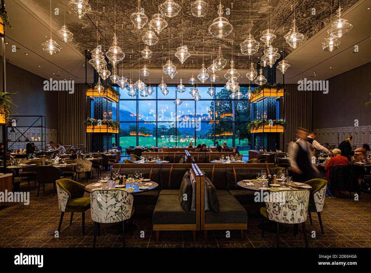The dining room of The Grill restaurant at the Dunloe Hotel & Gardens near Killarney, Ireland, offers a view of the Gap of Dunloe through a floor-to-ceiling window. A waiter hurries between the tables. Stock Photo
