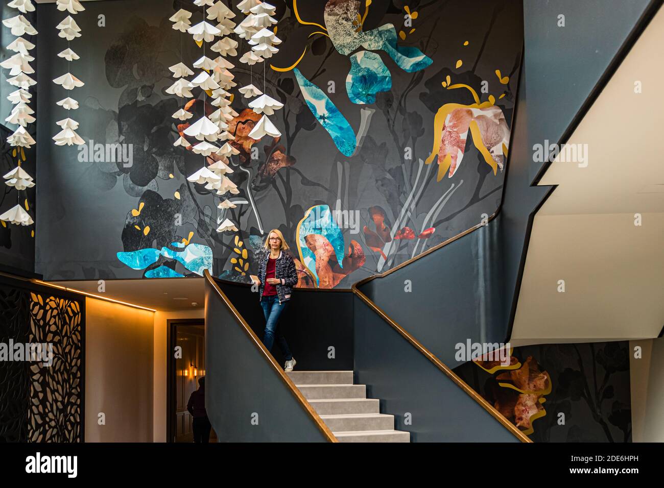 Journalist Angela Berg descends the staircase beneath a floral wall mural hung with paper blossoms at the Dunloe Hotel & Gardens near Killarney, Ireland. Stock Photo