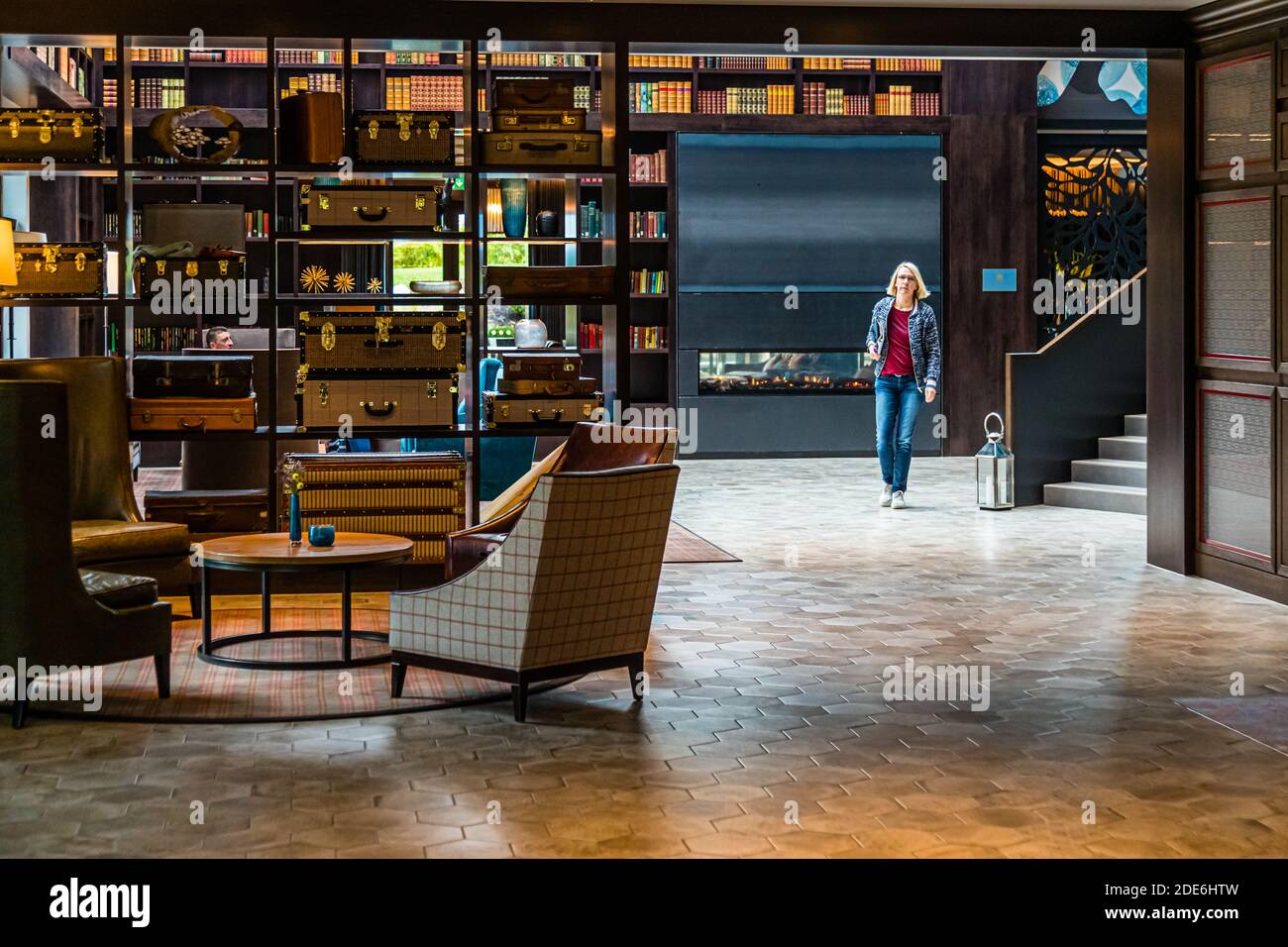 Journalist Angela Berg walks through a lounge at the five-star Dunloe Hotel & Gardens near Killarney, County Kerry, Ireland, featuring a fireplace built into the bookshelves and decoratively stacked vintage suitcases. Stock Photo