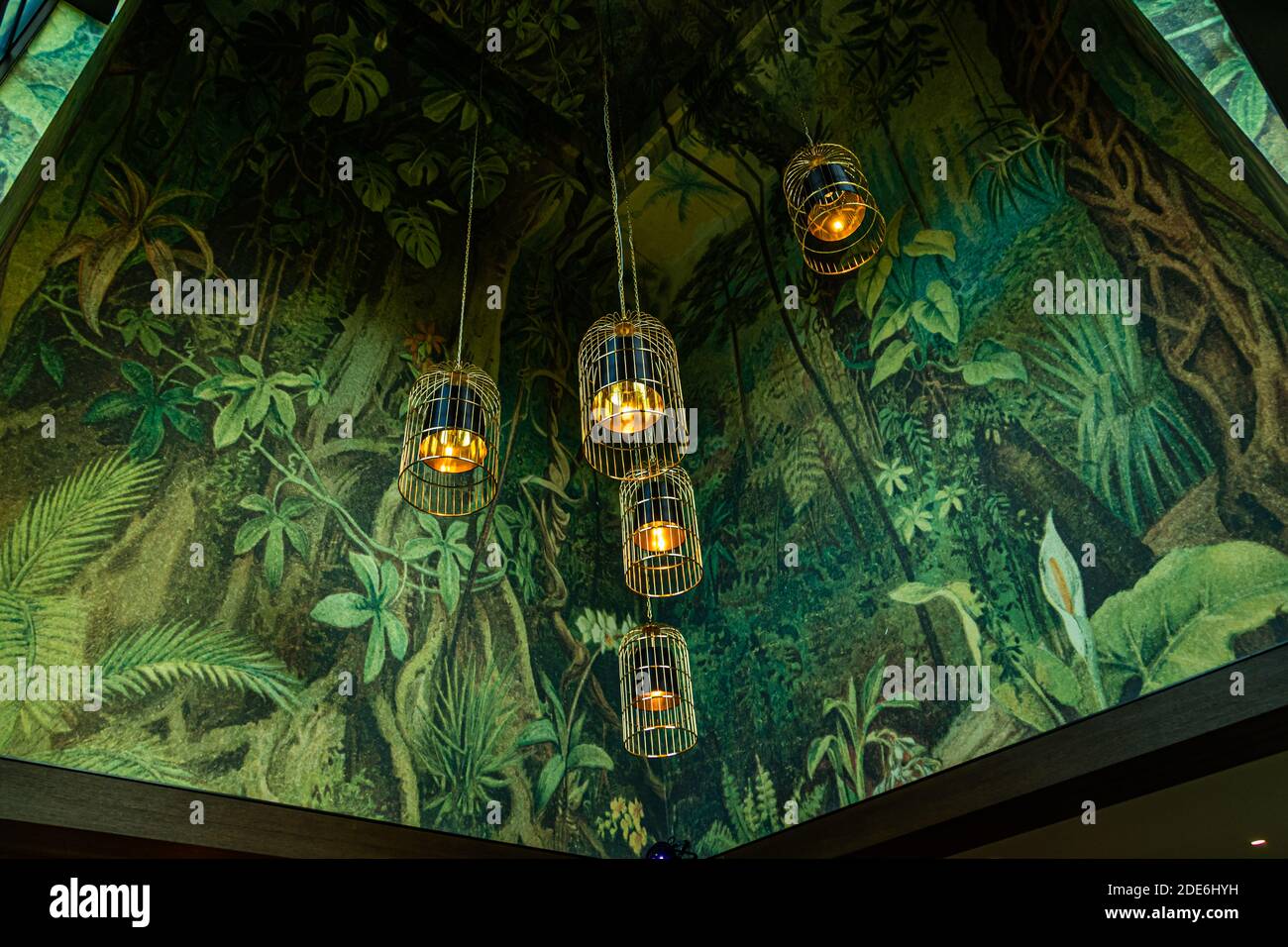 Cage-style pendant lamps with warm candlelight hang from a ceiling painted with a jungle motif at the five-star Dunloe Hotel & Gardens near Killarney, County Kerry, Ireland. Stock Photo
