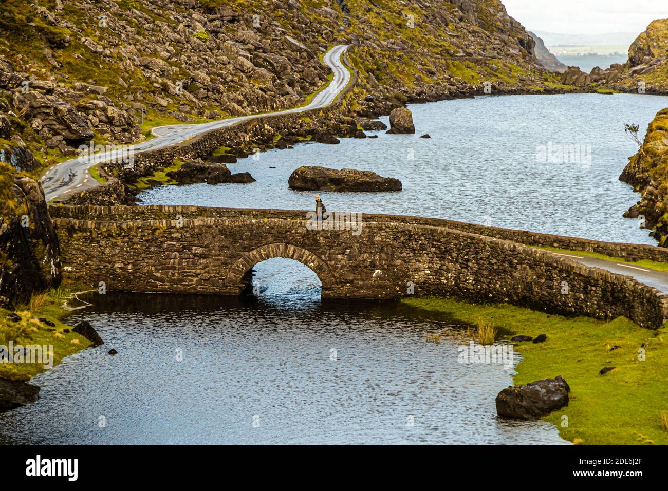 Large boulders sit in the water in front of the Wishing Bridge in the Gap of Dunloe near Killarney, County Kerry, Ireland. The winding mountain road runs along the shore of Coosaun Lough. Stock Photo
