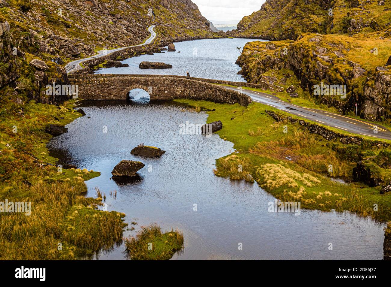 A hiker stands on the Wishing Bridge in the Gap of Dunloe near Killarney, County Kerry, Ireland, which spans the stream between Coosaun Lough and Black Lake. Stock Photo